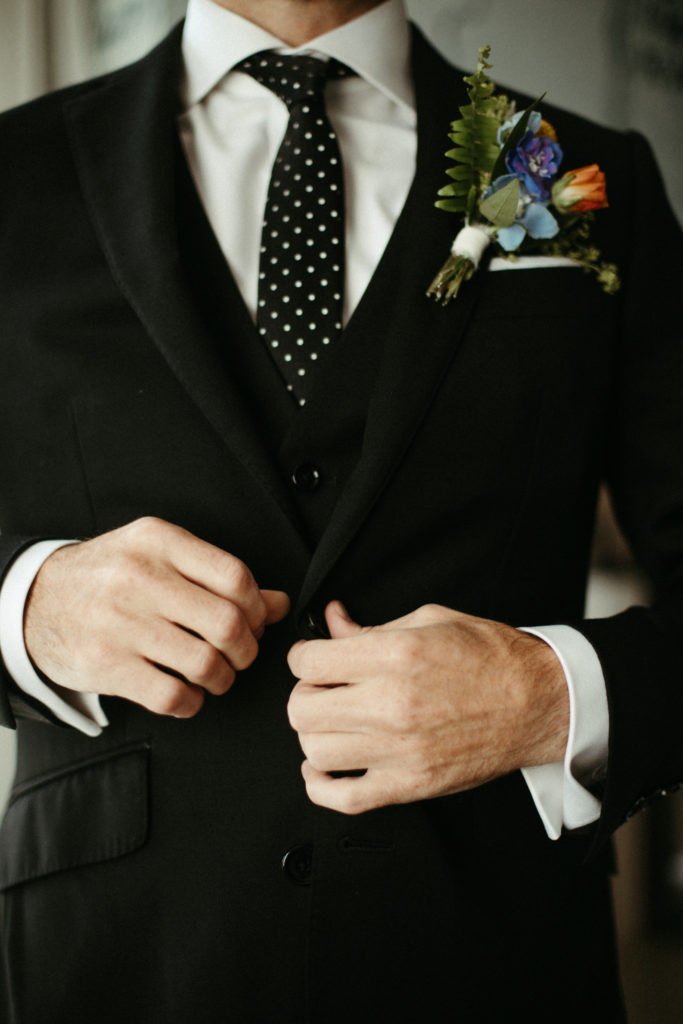 A groom buttoning up his suit jacket.