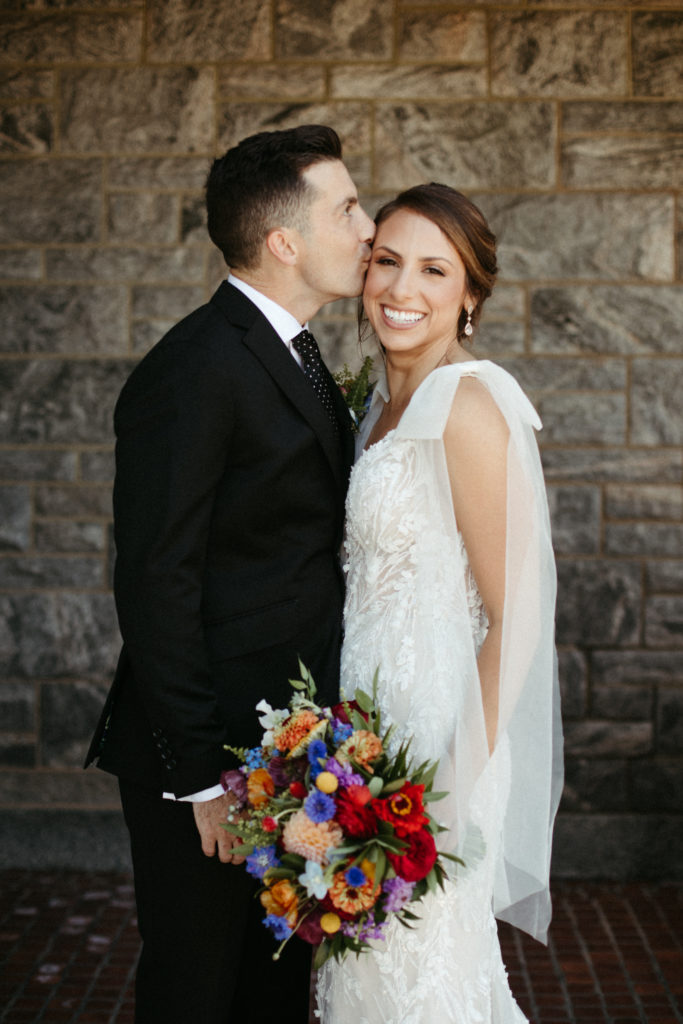 A groom kissing his bride on the cheek.