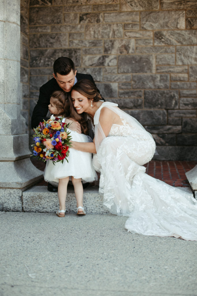 A bride and groom hugging their flower girl.