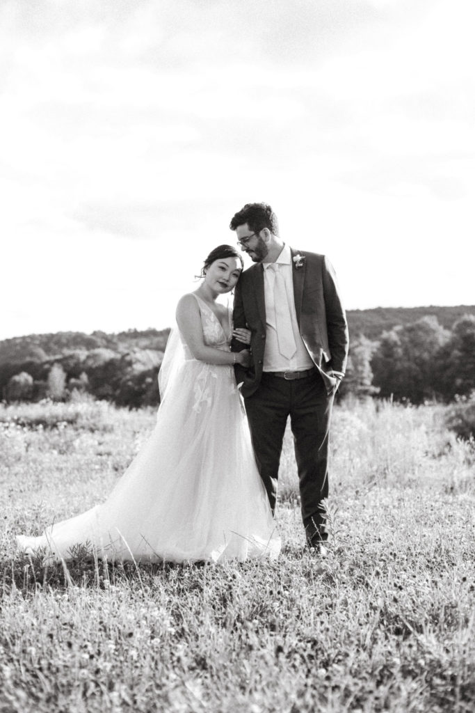 A bride and groom in a field of wildflowers with mountains in the background.