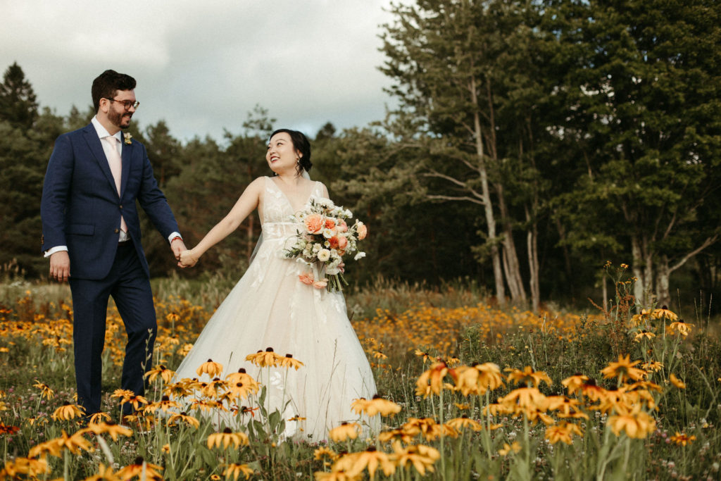 A bride and groom in a field of wildflowers with mountains in the background.