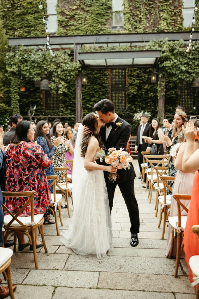 A couple exchanges vows in The Foundry's sunlit courtyard, surrounded by lush greenery and florals by Bad Boss Bride.