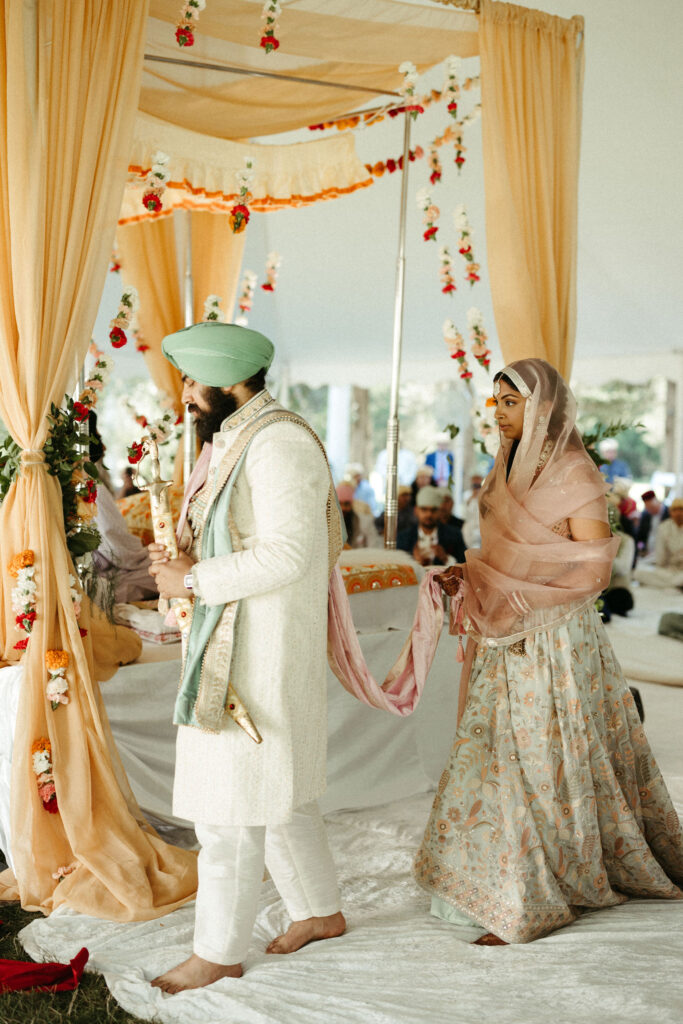 Bride and groom encircling the Guru Granth Sahib during the Laavan ceremony, surrounded by loved ones.
