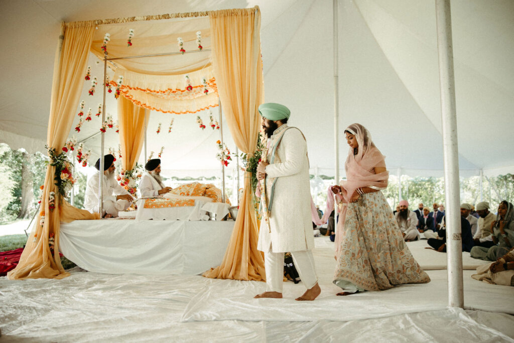Bride and groom encircling the Guru Granth Sahib during the Laavan ceremony, surrounded by loved ones.