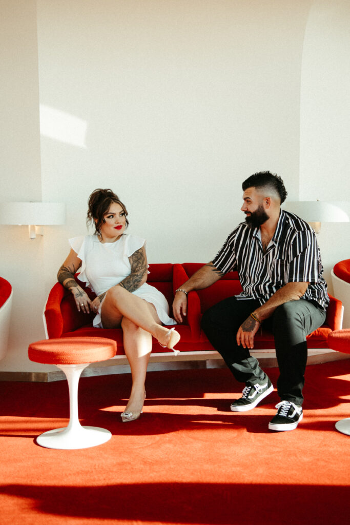 A stylish engagement session in the red-carpeted lounge of the TWA Hotel, highlighting its vintage design.