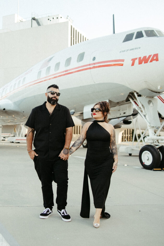 Engaged couple posing on the tarmac, capturing the vintage aviation vibes of the TWA Hotel.