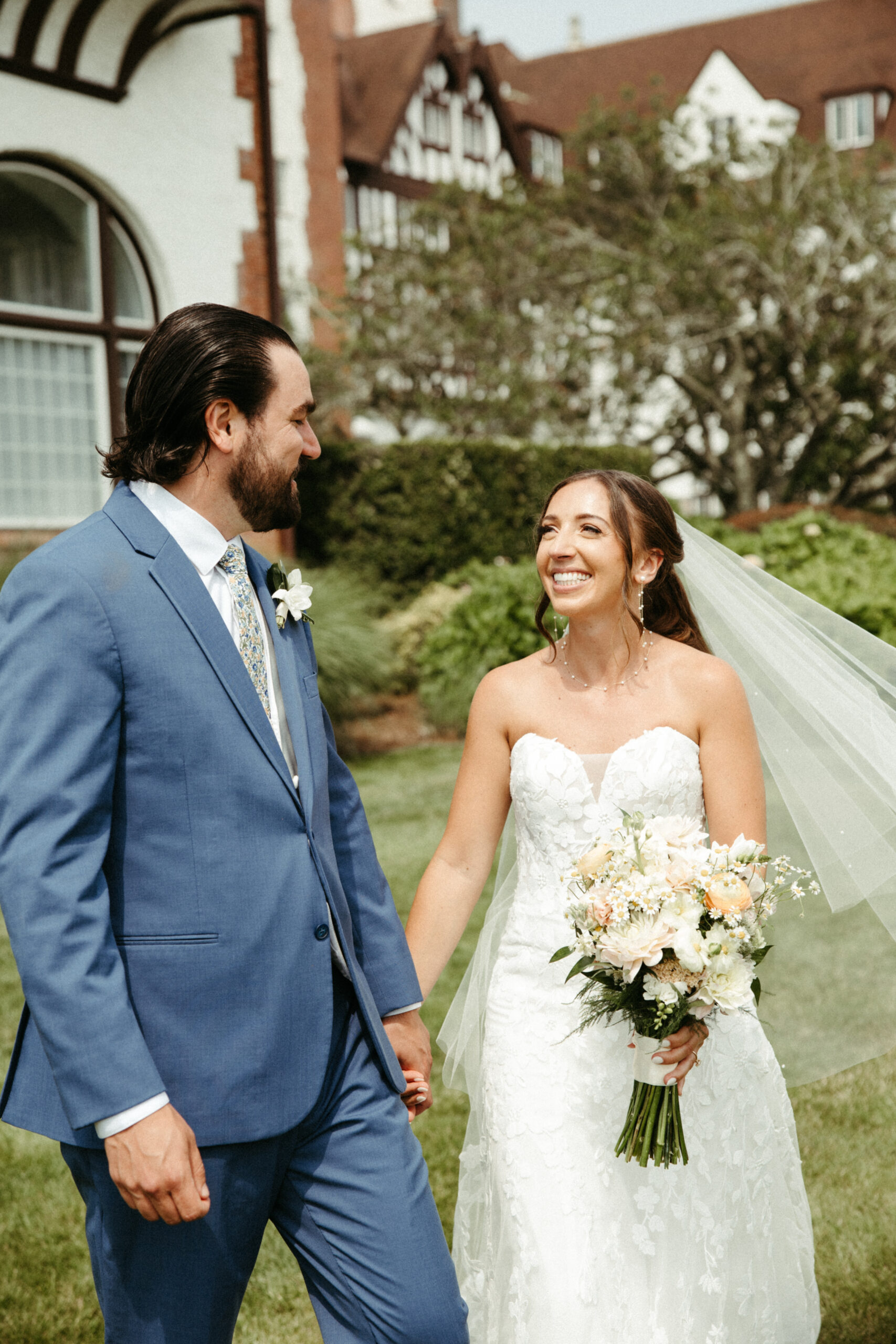 The couple stands hand-in-hand in front of the grand Montauk Manor.