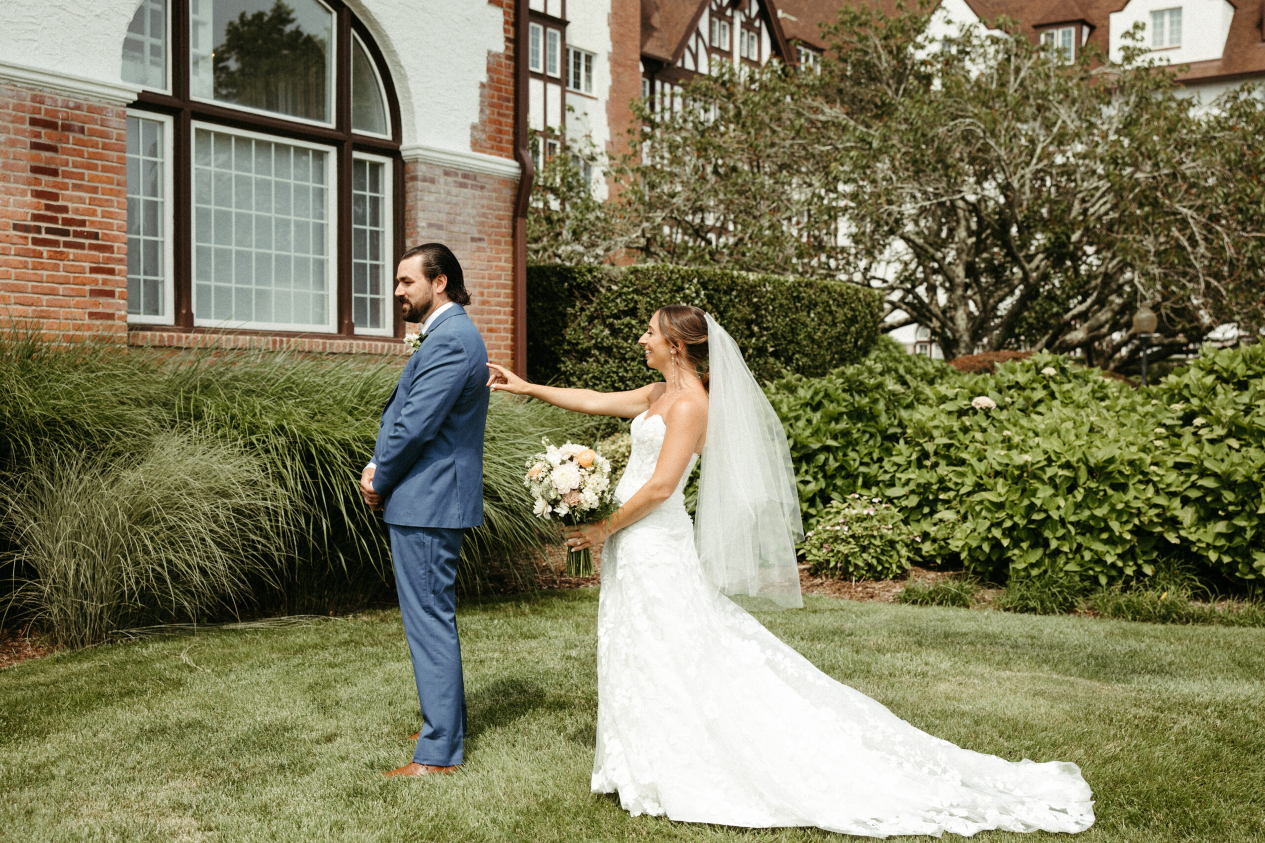 A bride approaches her groom for their first look, her veil trailing behind as he waits with anticipation.
