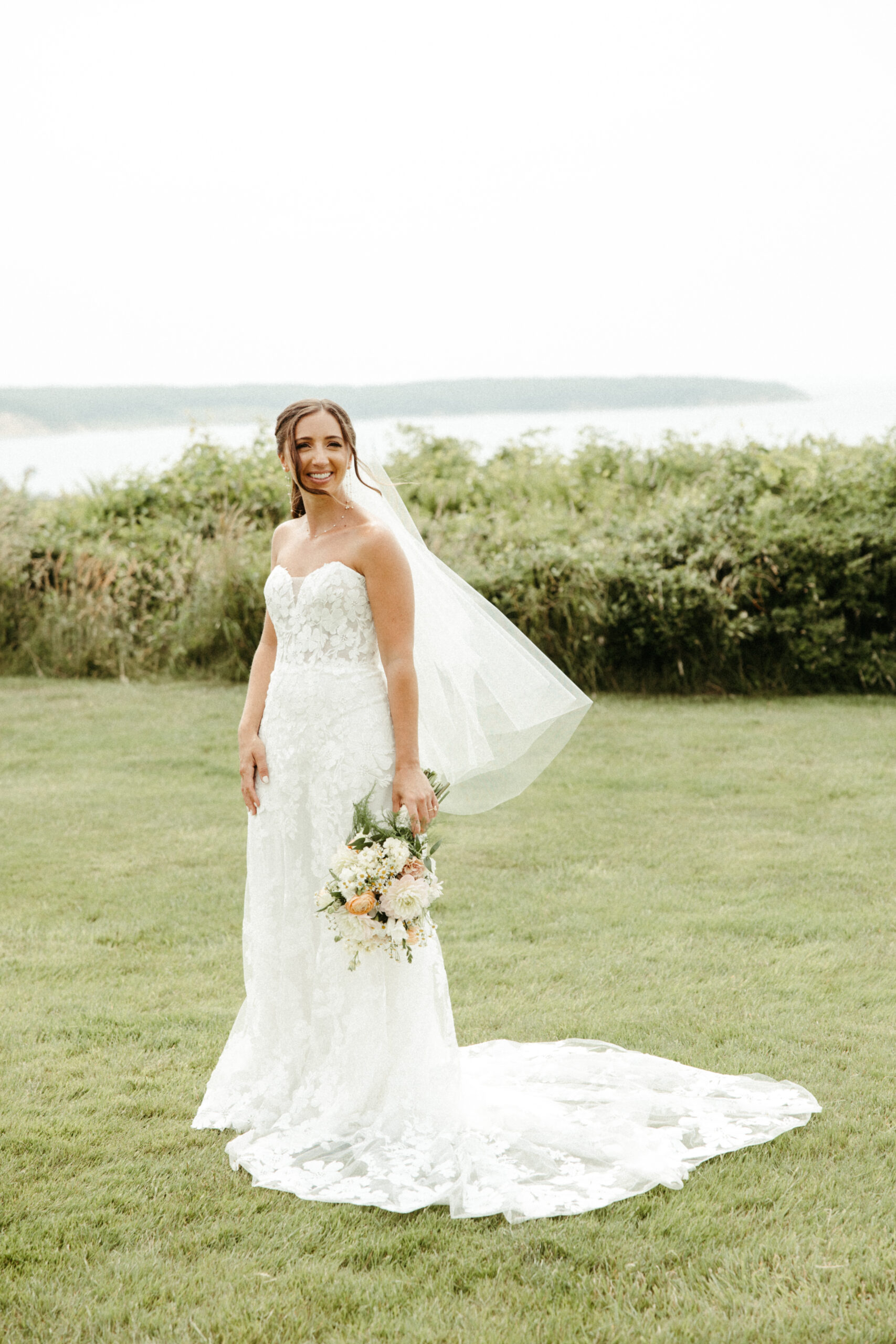 An unposed moment of bride standing with a view of Camp Hero in the background and the wind catching her veil.