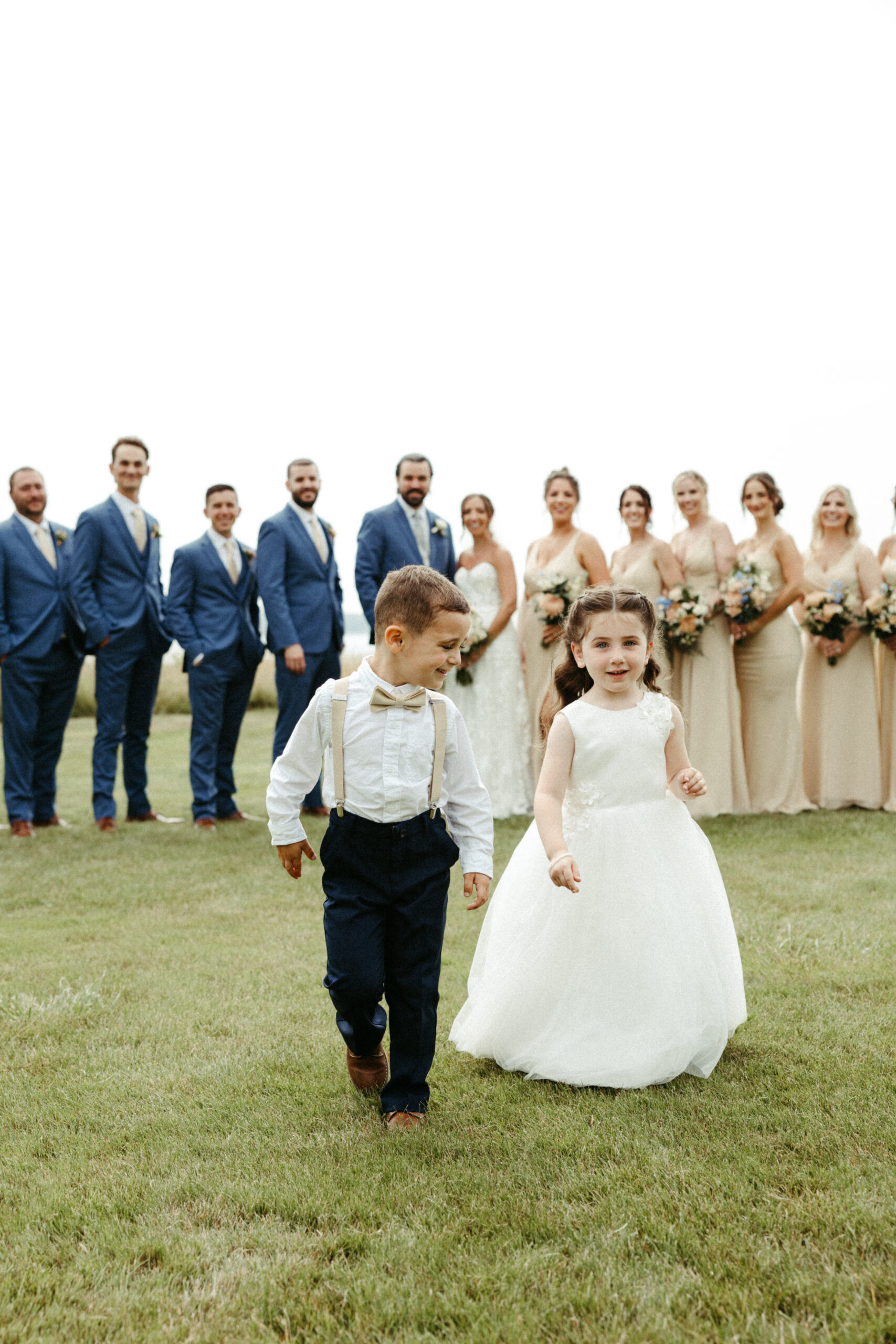 A flower girl and ring bear run away laughing from group photos.