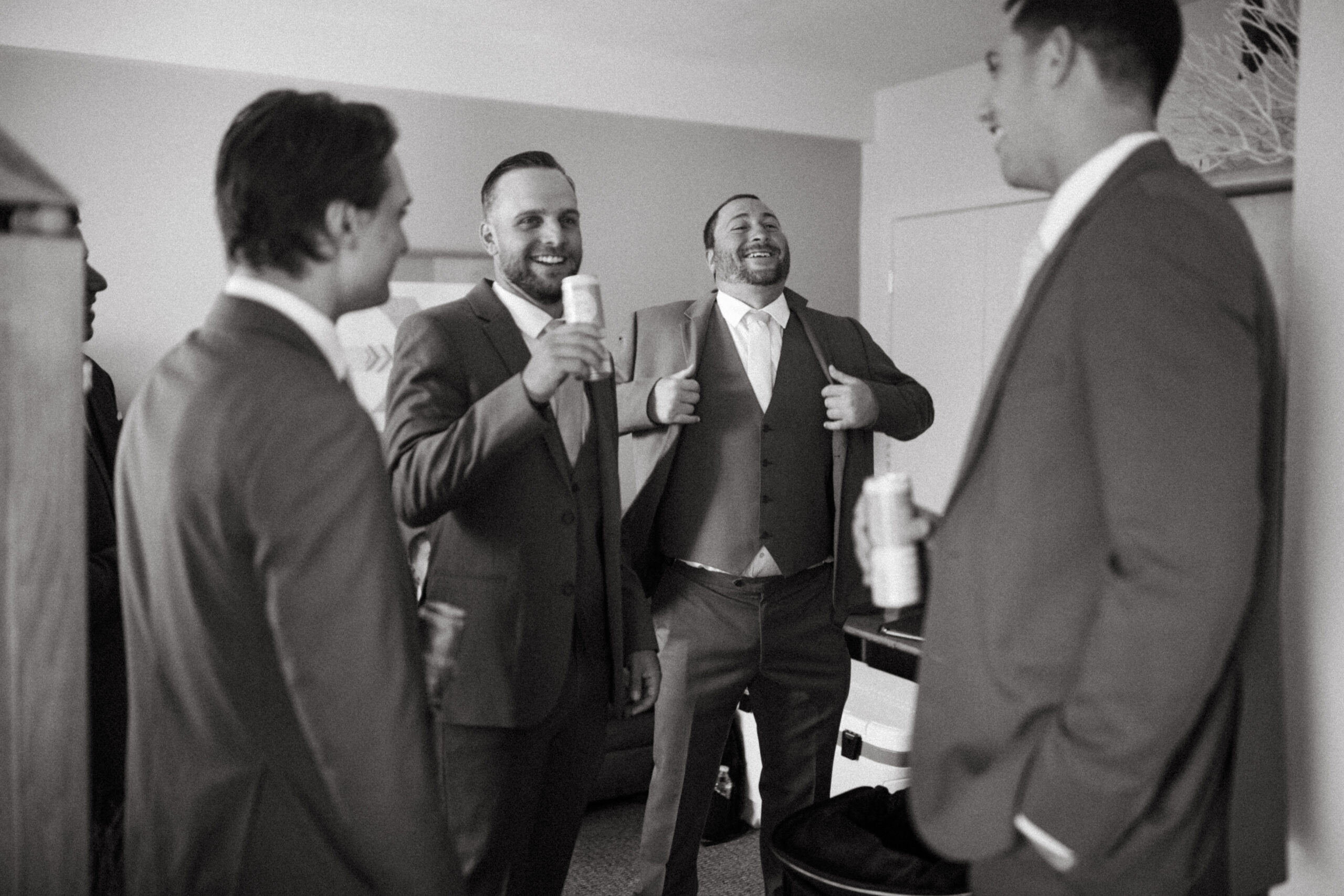 Groomsmen share laughs  while sharing a beer in a moment of joy before the ceremon