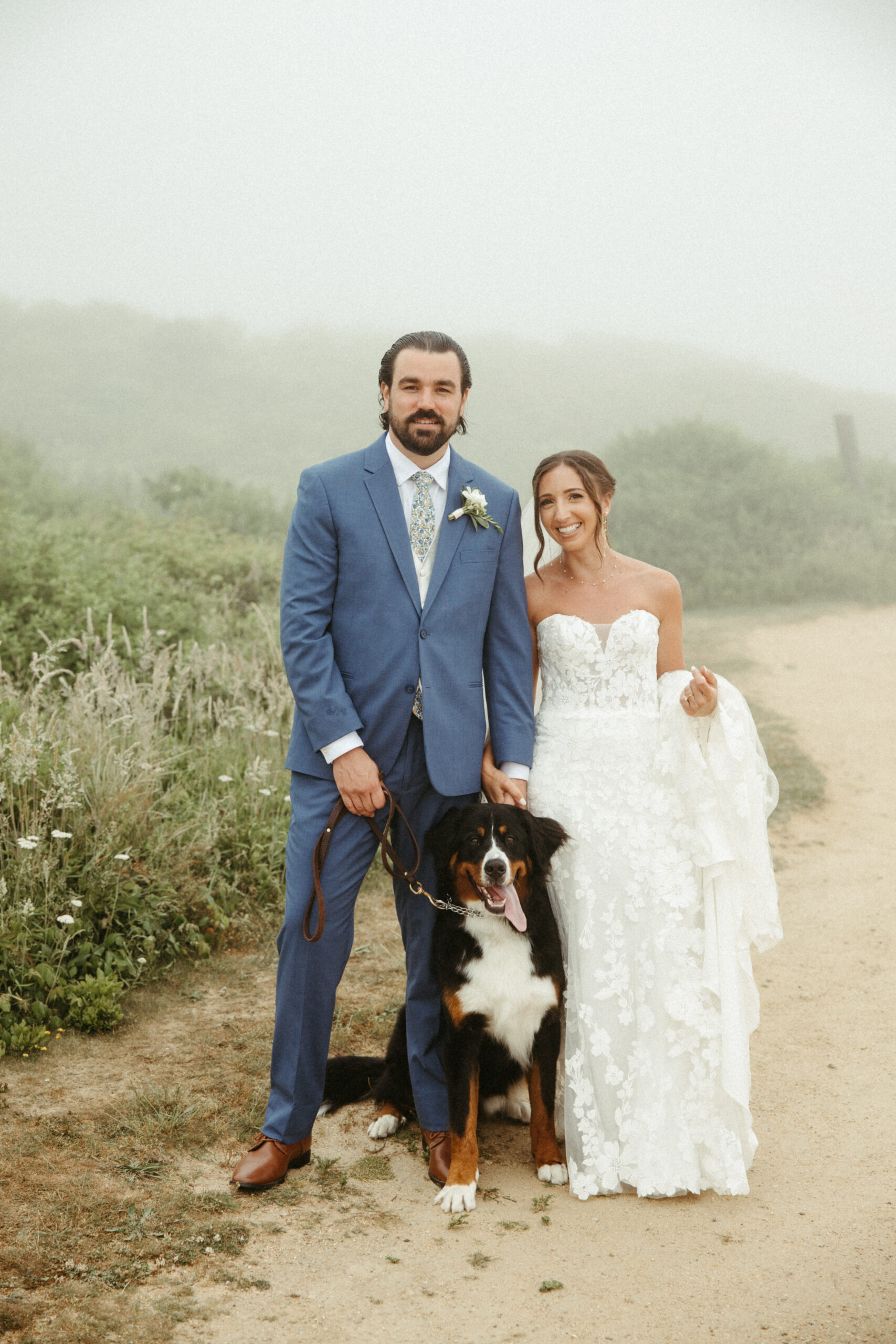 Their Burmese mountain dog, with his tongue hanging, nuzzles tthe couple, all smiling for a photo.