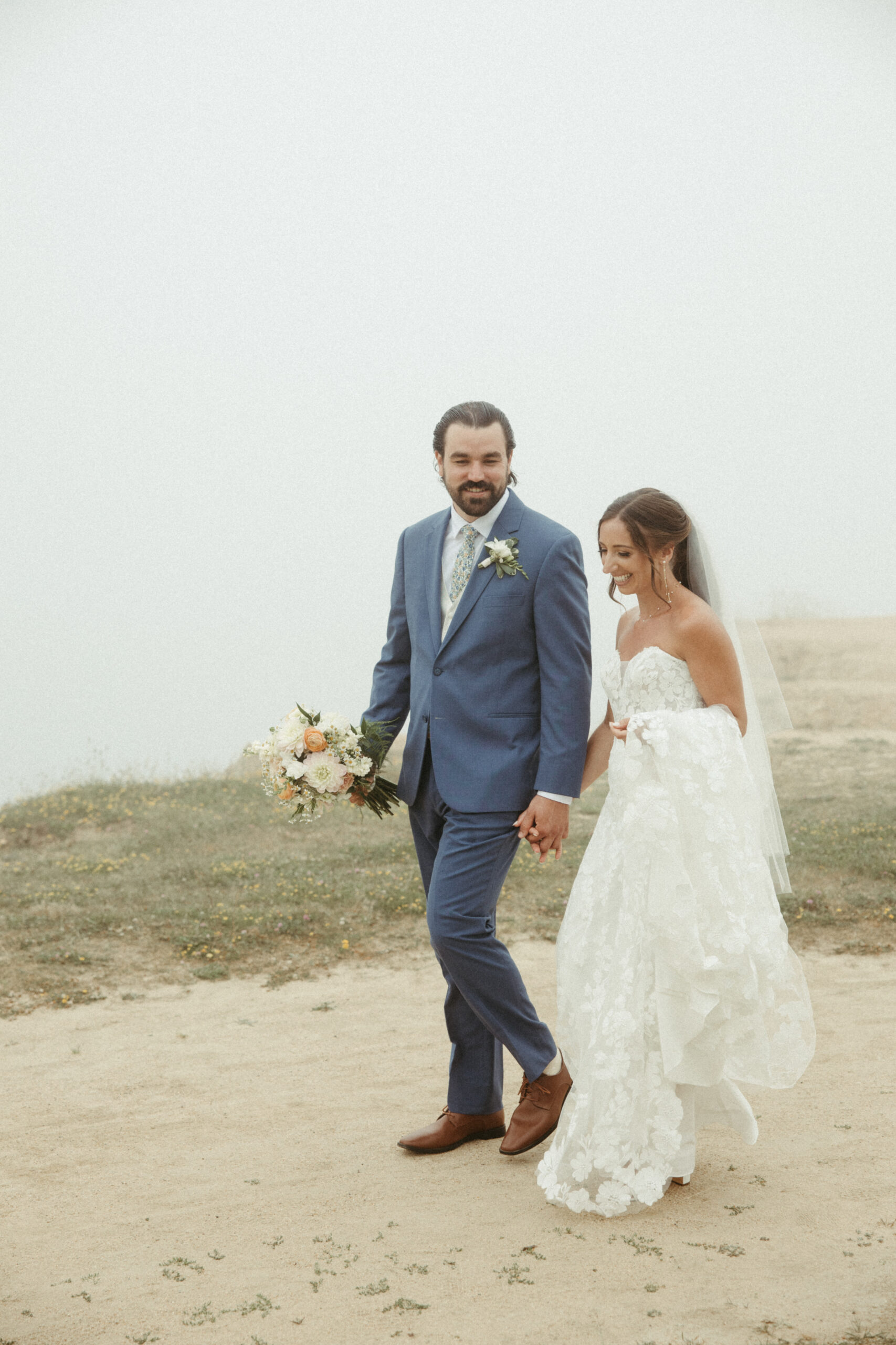 The newlyweds walk hand-in-hand along the rugged Montauk cliffs the mist blocking the ocean below.