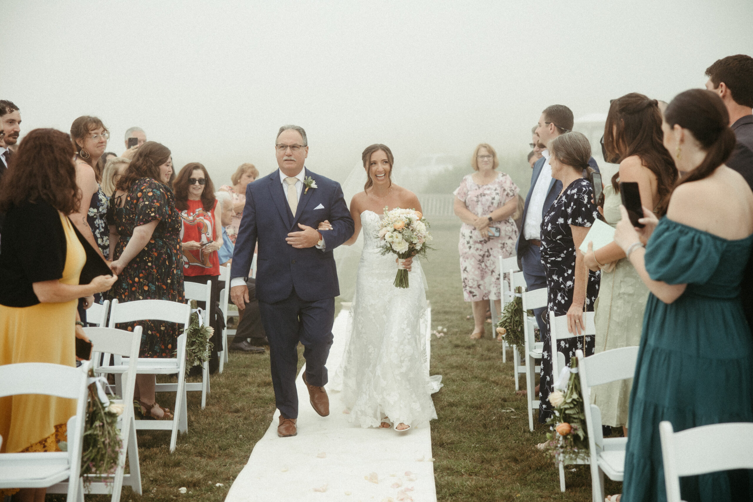 The bride steps forward through the fog, her dress flowing.