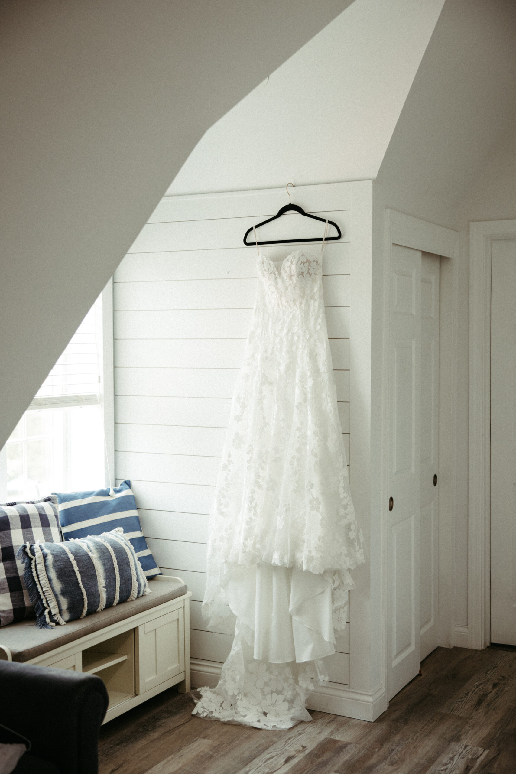 A flowing wedding gown hangs by a sunlit window at Montauk Manor, the delicate lace catching the morning light.