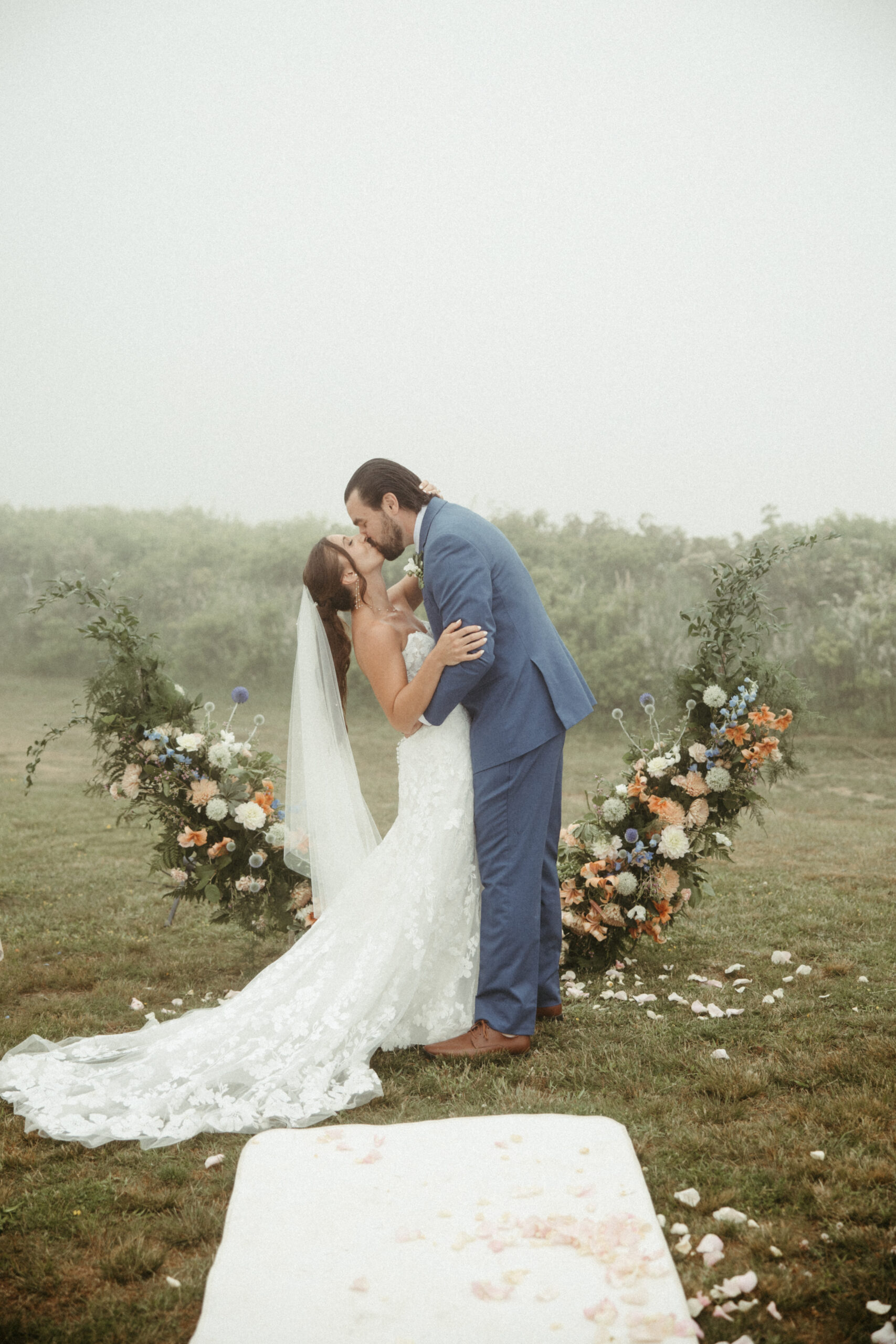 The newlyweds share their first kiss, the fog creating an intimate, cinematic backdrop.
