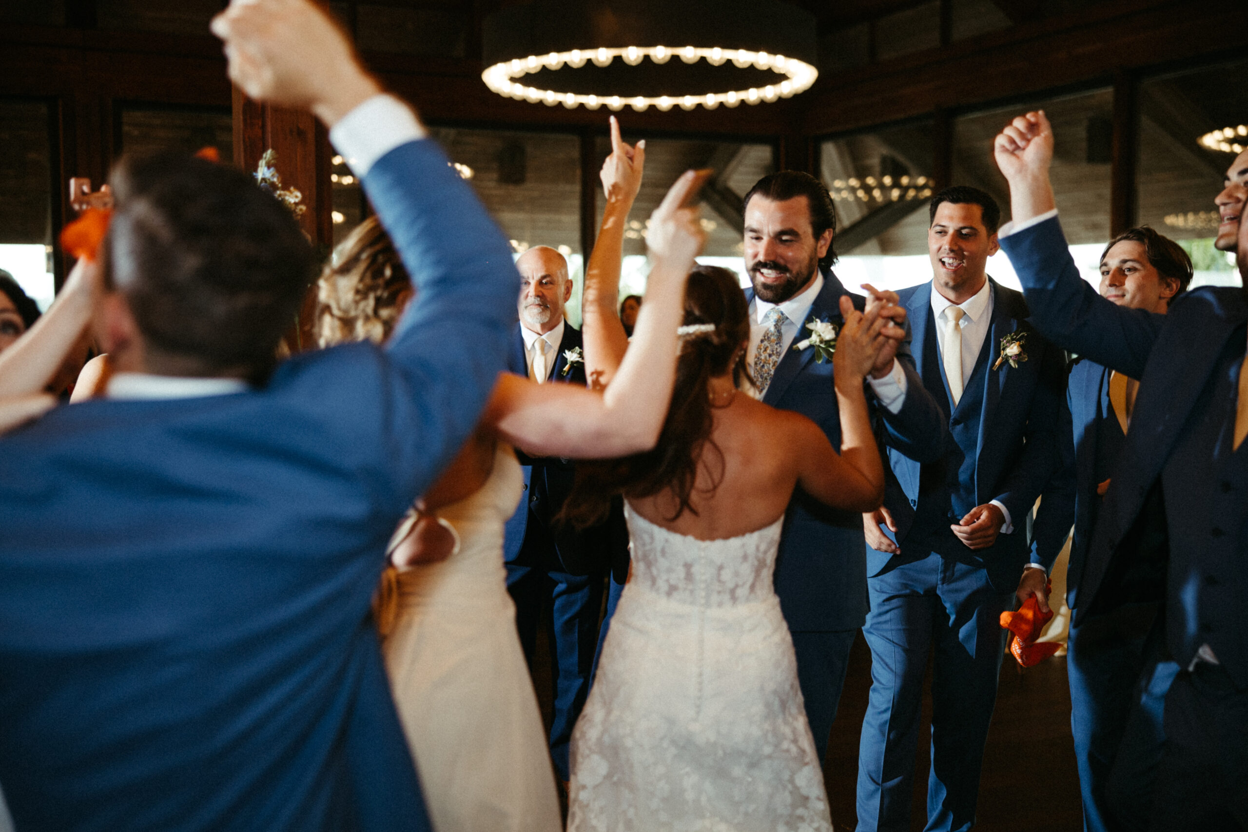 Guests twirl and laugh on the dance floor, hands raised in celebration.
