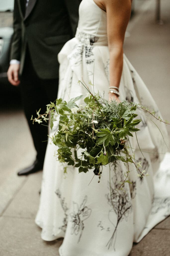 Bride holding a wild greenery bouquet with her floral wedding dress flowing during her Houston Hall NYC wedding