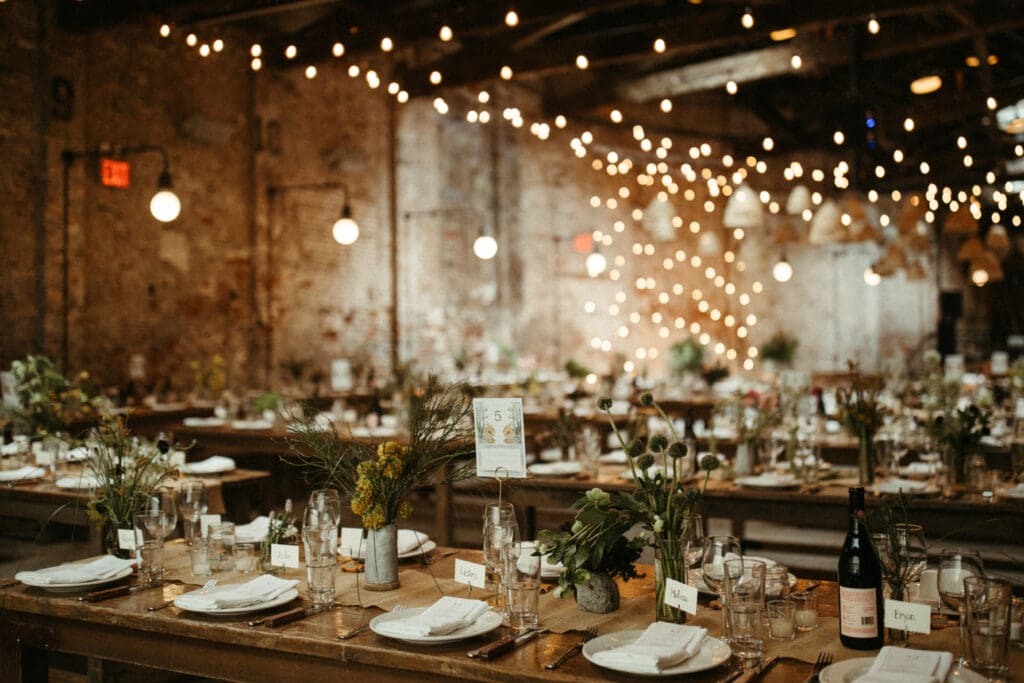 Rustic reception tables inside Houston Hall in New York City, styled with wildflower centerpieces, candles, and glowing bistro lights for a romantic industrial wedding.