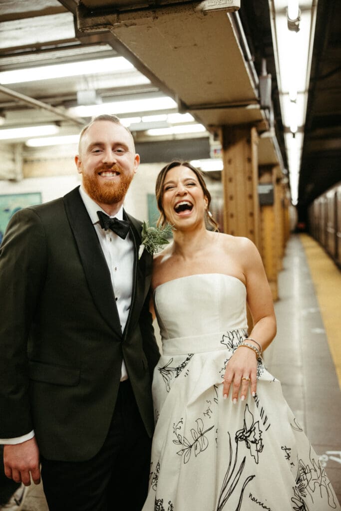 Bride and groom laughing together on a Houston Street subway platform after their New York City wedding