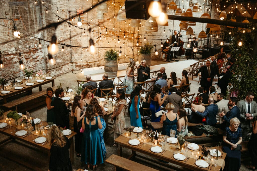 Wedding ceremony setup inside Houston Hall in NYC with string lights, exposed brick walls, and live musicians creating a romantic atmosphere