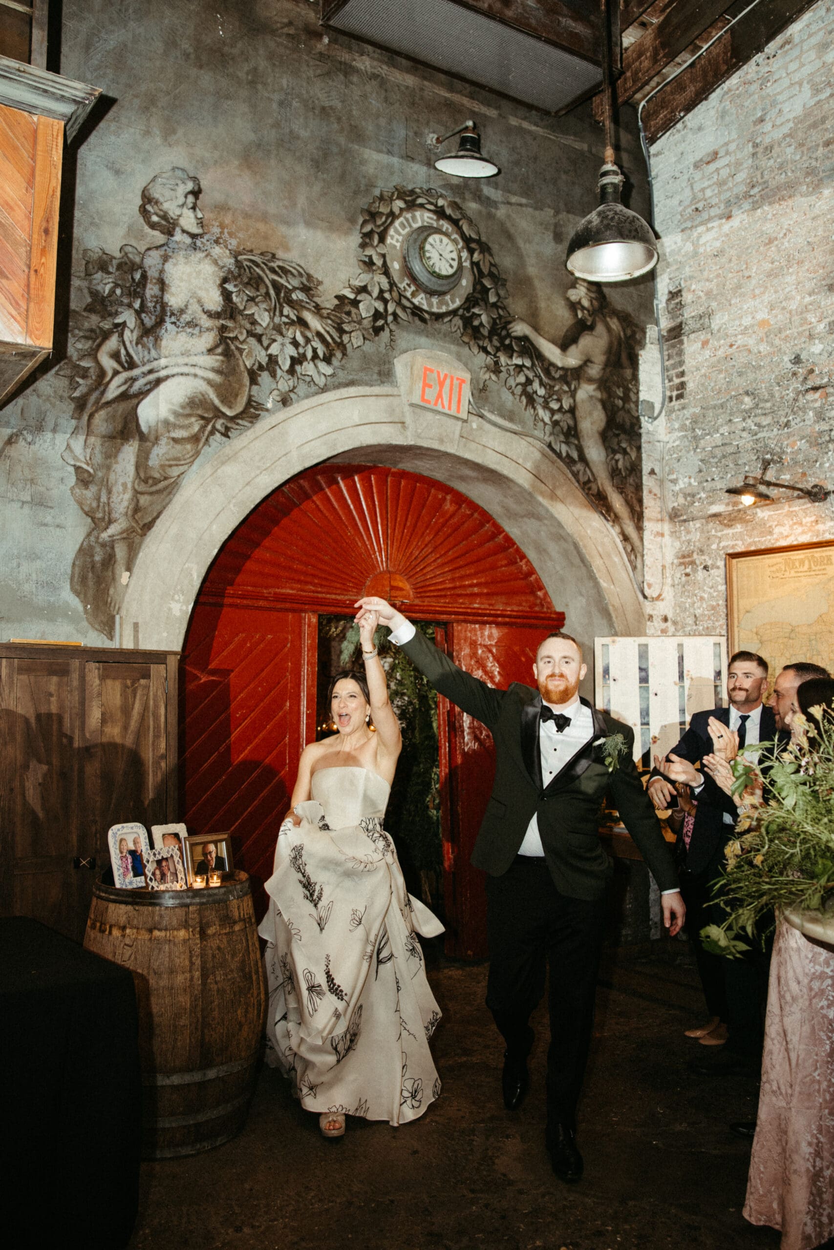 Bride and groom entering their Houston Hall wedding reception through the red arched doors as guests cheer inside the candlelit NYC venue