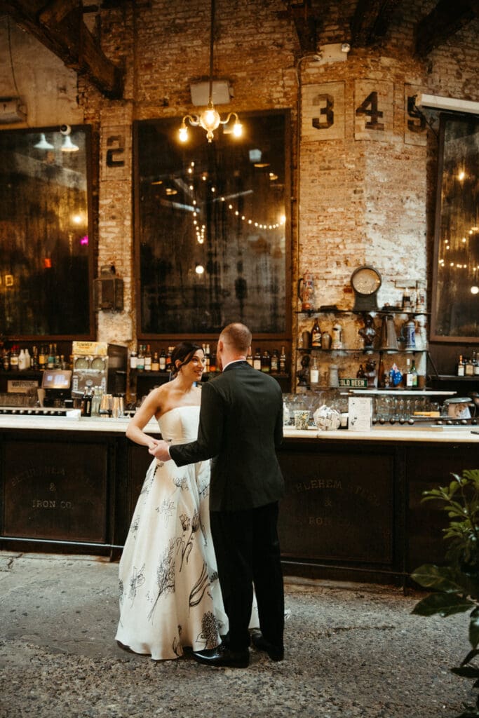 Bride and groom sharing a moment at the bar inside Houston Hall, an industrial New York City wedding venue with warm ambient lighting