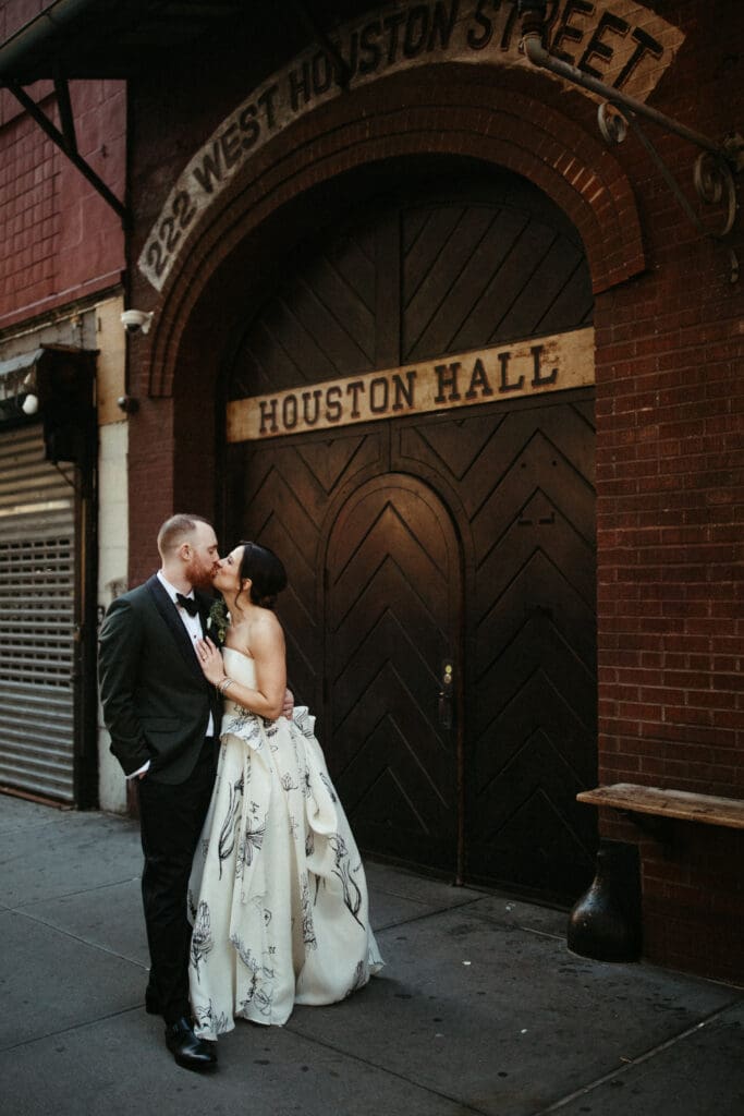 Bride and groom kissing outside Houston Hall in the West Village, a classic New York City wedding venue with historic brick and arched doors