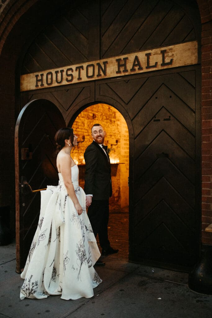 Newlyweds walking through the iconic Houston Hall doors in New York City, stepping into their wedding reception in a warm candlelit space