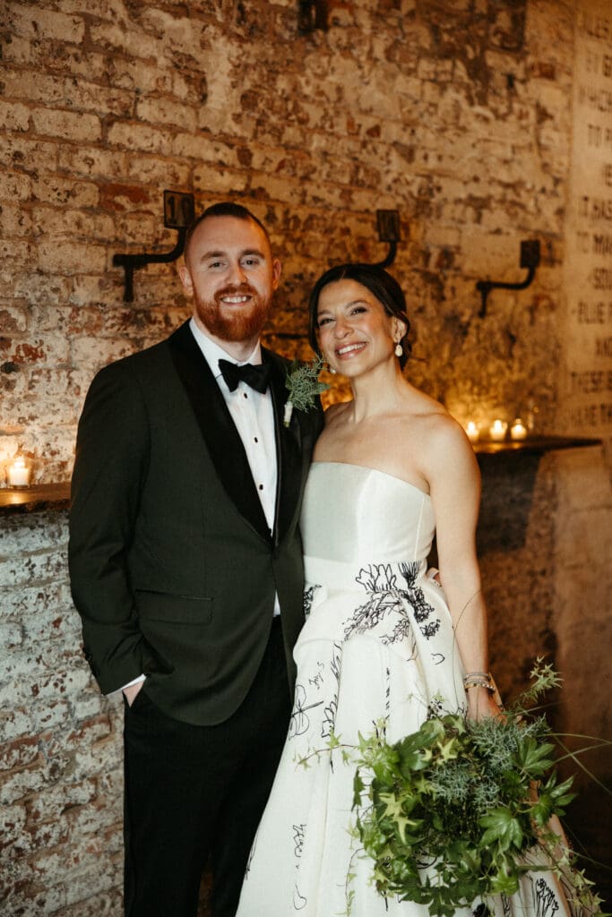 Bride and groom smiling together inside Houston Hall with exposed brick and candlelight during their New York City wedding