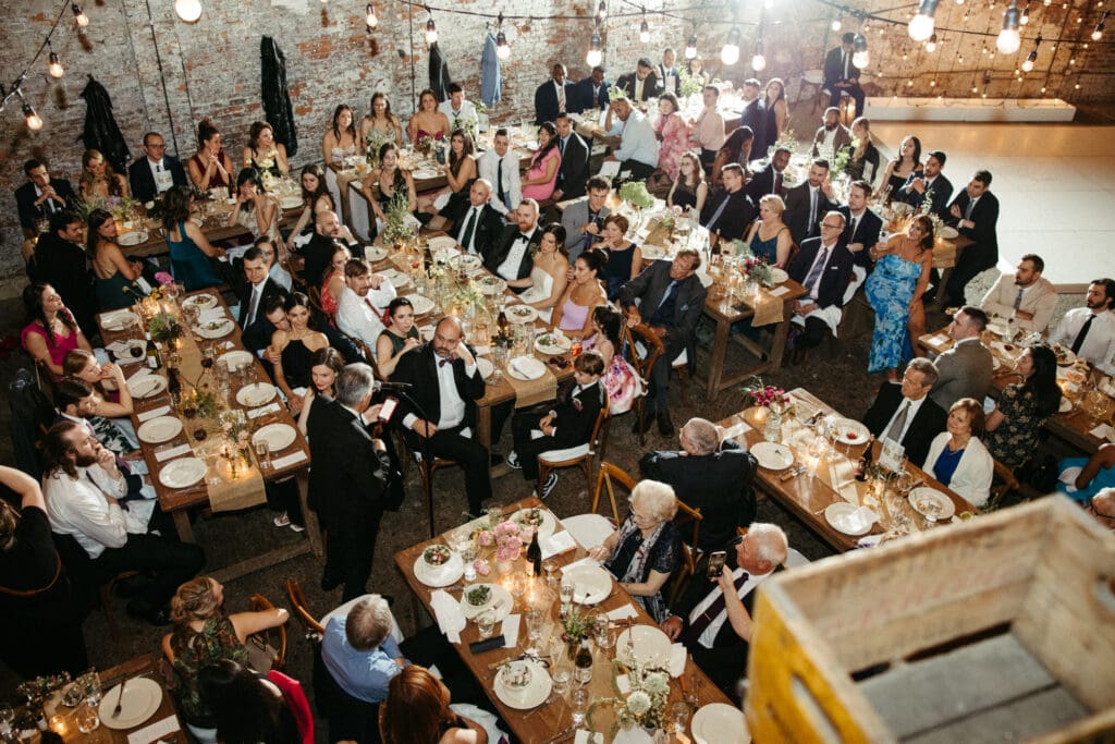 Guests gathered inside Houston Hall during a lively New York City wedding reception with long tables, candlelight, and industrial charm
