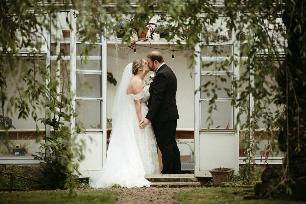 Bride and groom kiss in the doorway of the greenhouse during their first look at Stone Acres Farm