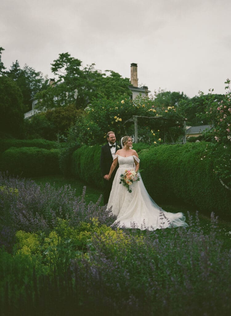Bride and groom walking hand in hand through lavender and wildflowers at Stone Acres Farm, captured on film during their wedding portraits.