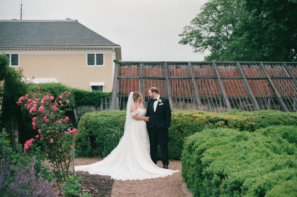 Bride and groom standing together along a garden path at Stone Acres Farm with the greenhouse behind them, photographed on film.